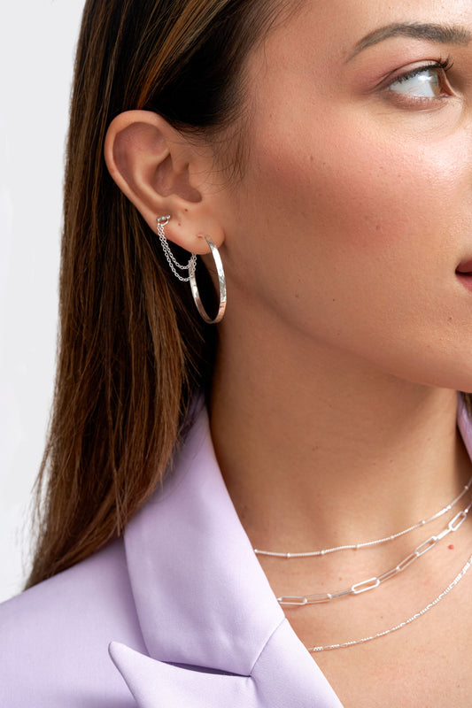 Woman wearing Sterling Silver large earring hoops with a hammered finish and a lab grown diamond stud. Both joined with a double chain earring connector.. L'ERA Jewellery