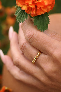 Hand wearing a gold ring with an orange flower in the background