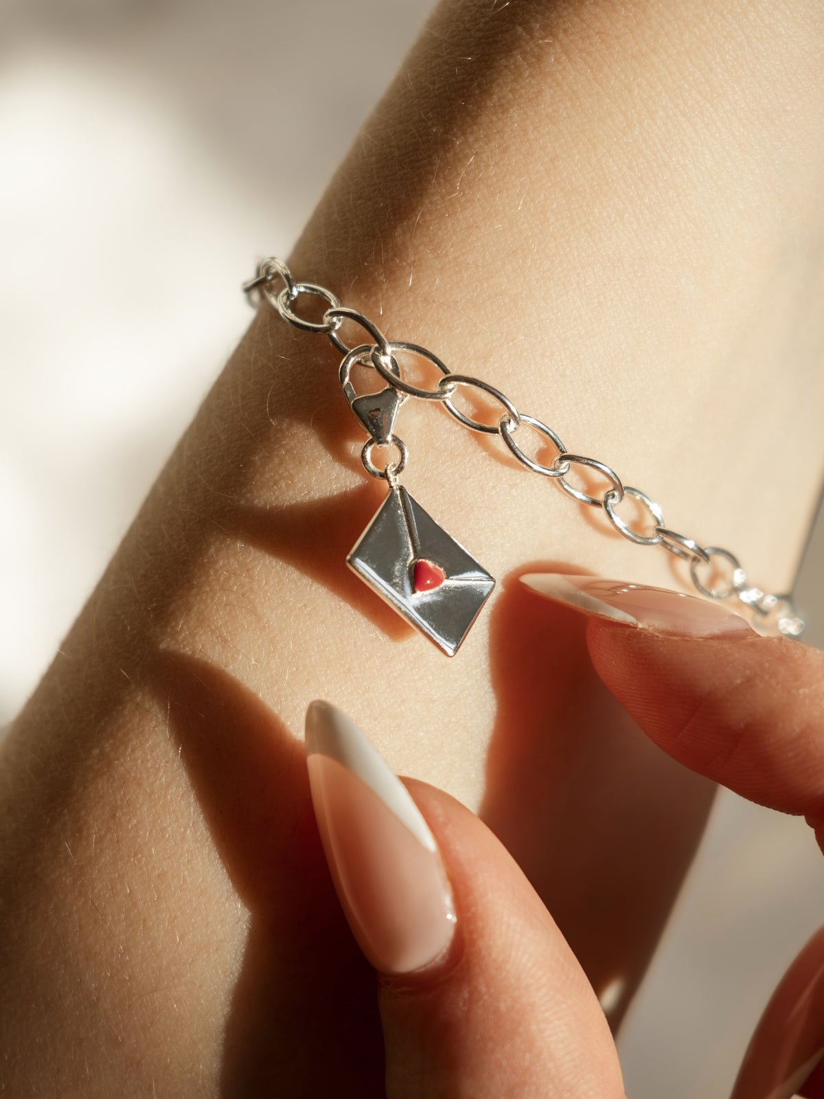model wearing enamel letter charm with red heart on bracelet in silver